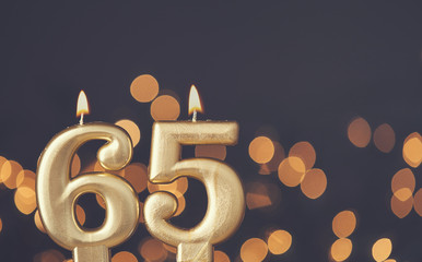 Gold number 65 celebration candle against blurred light background