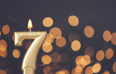 Gold number 7 celebration candle against blurred light background