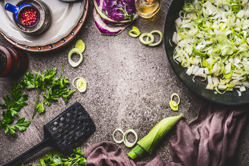 Leeks meal eating and cooking . Pan with sliced leeks on kitchen table background with tools and ingredients, top view, frame