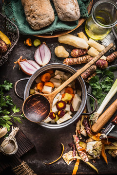 Cooking pot with wooden spoon and vegetables on rustic kitchen table background. Homemade healthy food and eating or vegetarian concept