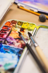 Details of the creative process of the artist, a palette with watercolor paints, brushes and canvas with a sketch.