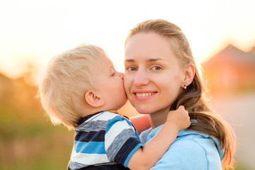 Woman and child outdoors at sunset. Boy kissing his mom.