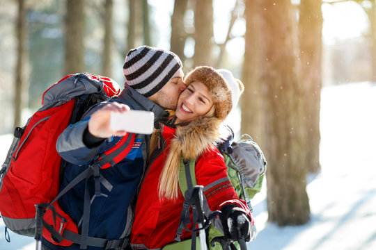 Male mountaineer kissing his girlfriend while making selfie on winter