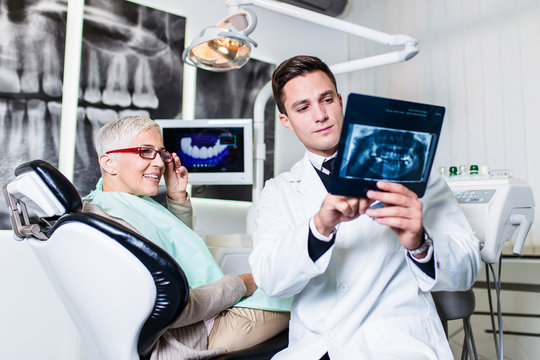 Handsome smiling dentist looking at x-ray image of his senior woman patient. 