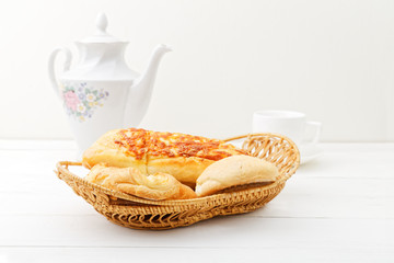 Wicker basket with fresh pastry on white wooden table.
