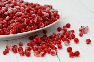 Closeup of frozen redcurrants on white ceramic plate on white painted table. Spilled currants.