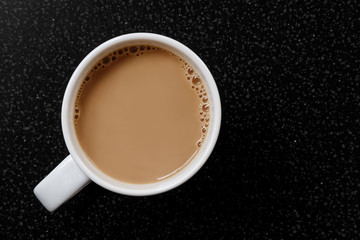 White coffee or tea with bubbles in white ceramic mug isolated on black granite table from above.