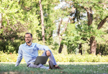 Obraz premium Elegant man with laptop sitting in park