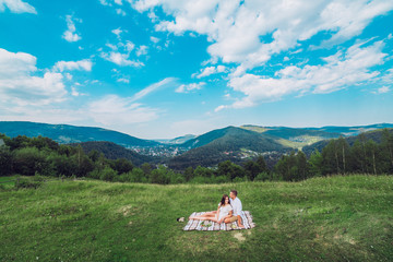 Fototapeta na wymiar Young couple in love resting on peak of mountain in summer. Couple spreading a blanket for picnic