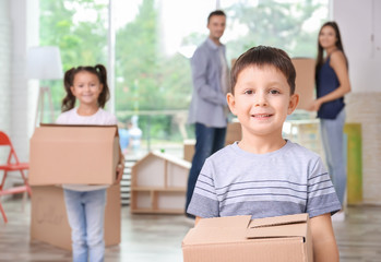 Cute little boy with moving box in room at new home