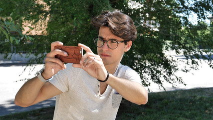 Handsome young man in city park taking photos with cell phone