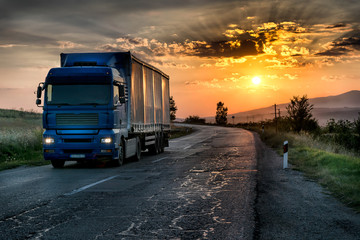 Obraz premium Blue lorry on the asphalt rural road in a beautiful sunset
