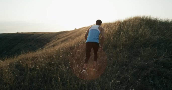 Male jogger training for marathon run running up hill in silhouette against colorful yellow sky. Fit fitness model living healthy active outdoor lifestyle. 4k