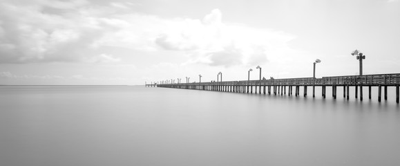 Obraz premium Long exposure wooden fishing pier stretching out over Galveston Bay in La Porte, Texas, USA. Foot pier for saltwater fishing with motion blurred people, recreation concept. Panorama nature seascape