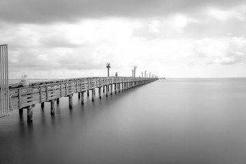 Long exposure wooden fishing pier stretching out over Galveston Bay in La Porte, Texas, USA. Foot pier for saltwater fishing with motion blurred people, recreation concept. Nature seascape background © trongnguyen
