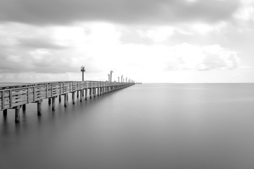Obraz premium Long exposure wooden fishing pier stretching out over Galveston Bay in La Porte, Texas, USA. Foot pier for saltwater fishing with motion blurred people, recreation concept. Nature seascape background