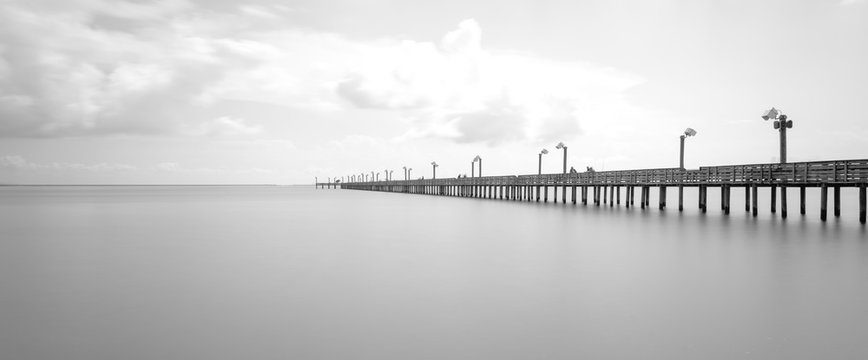 Fototapeta Long exposure wooden fishing pier stretching out over Galveston Bay in La Porte, Texas, USA. Foot pier for saltwater fishing with motion blurred people, recreation concept. Panorama nature seascape