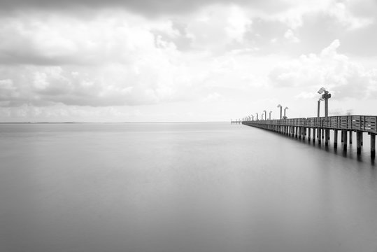 Fototapeta Long exposure wooden fishing pier stretching out over Galveston Bay in La Porte, Texas, USA. Foot pier for saltwater fishing with motion blurred people, recreation concept. Nature seascape background