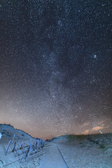 Wooden path in the sandy dunes. Night sky full of stars.