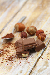 Pieces of crunchy chocolate with whole hazelnuts on rustic wooden surface
