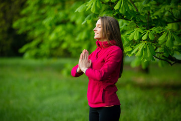 Healthy meditating inspired young woman standing on green park, copy space