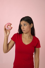 young beautiful latin woman in red with pink sugar donut thinking and feeling guilty after biting isolated