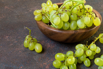 Branch of a green grapes on a wooden plate on a dark background with copy space and selective focus