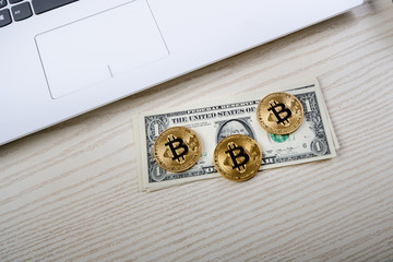 Bitcoin golden coins on a table with dollar banknotes and laptop. Virtual money. Cryptocurrency business. Office background.