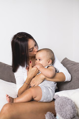 Beautiful mother enjoying and relaxing with her cute little baby on bed. 