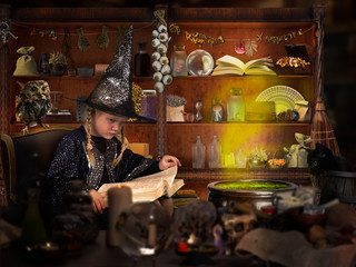The wizard of room. Little girl in witch hat reads a big book of spells. Many mystical items. The...