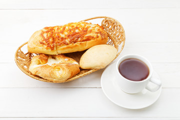 Wicker basket with fresh pastry and cup of tea on white wooden table.
