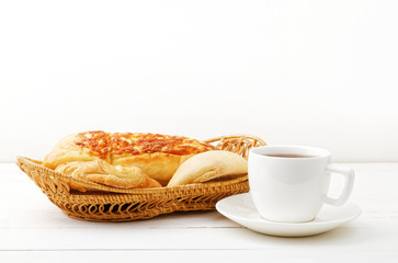 Wicker basket with fresh pastry and cup of tea on white wooden table.