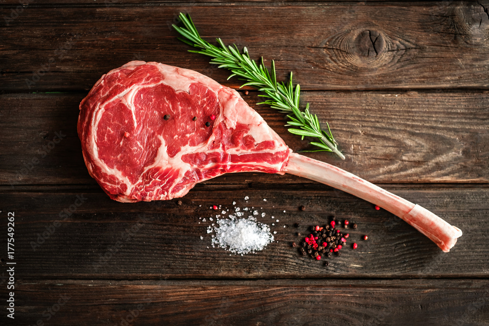 Wall mural raw tomahawk steak on wooden background with spices for grilling