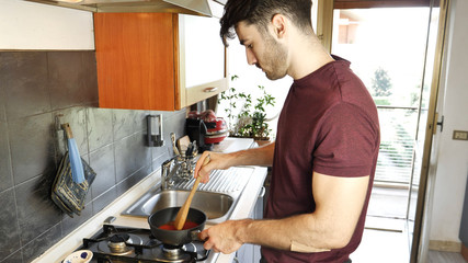 Young man cooking tomato sauce in kitchen