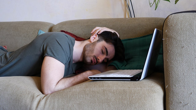 Tired Young Man Falling Asleep on Laptop Computer