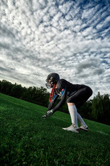Woman American football player took up a position on the field against the sky.