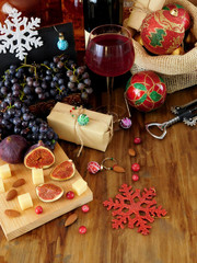 Cheese and figs on a wooden board, red wine in a glass, grape and Christmas attributes around. Christmas table laying