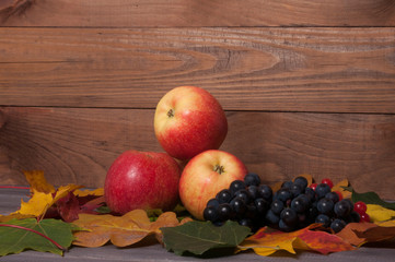 Beautiful juicy apples with grapes on a wooden table in autumn foliage