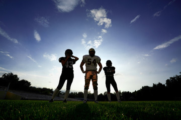 Players in American football are on the field against the sky at sunrise.