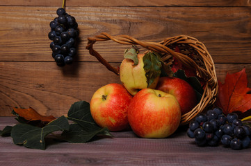 juicy apples in a basket on an autumnal wooden table with grapes