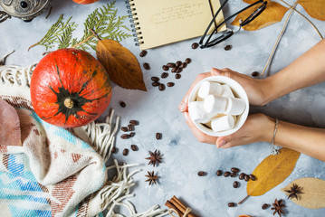Autumn background with cup of marshmallow, yellow maple leaves and pumpkins. women's hands hold a cup