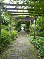 Corridoio con strutture di legno e piante lussureggianti nel giardino di Castillon in Normandia, Francia.