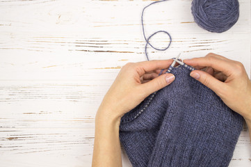 hand with the needles and a knitted cloth. on wooden white background