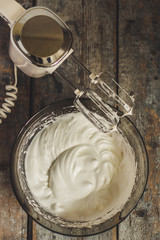 Whipped proteins in a bowl and mixer on a wooden surface