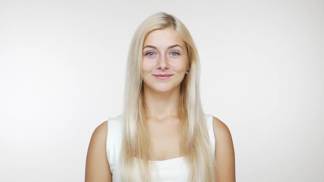 slow motion caucasian young blond blue-eyed girl looking at camera smiling over white background. Concept of emotions