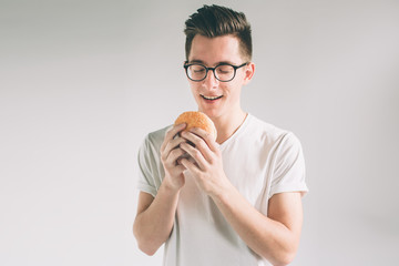 man holding hamburger. student eats fast food. not helpful food. very hungry man. Nerd is wearing glasses.