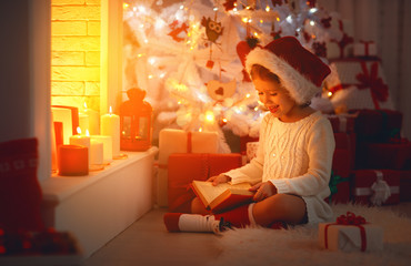 happy child girl read book at christmas near   fireplace at home.