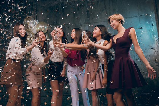Celebrating with fun. Group of cheerful young girls carrying champagne flutes and dancing in gold confetti. The best party in 2018 year. Happy New year!