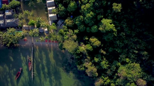 As aerial camera looks straight down at a seaside paradise resort, a fisherman&rsquo;s boat leaves the dock during sunrise.
