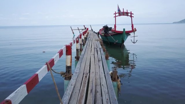 Moving forward onto the boat pier towards a fishing boat, the aerial camera continues up and over the railing.